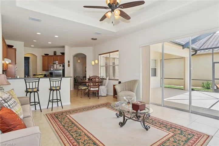 Living area with arched walkways, a ceiling fan, light tile patterned floors, recessed lighting, and a tray ceiling
