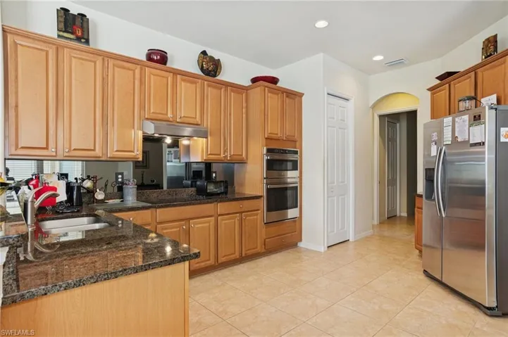 Kitchen with appliances with stainless steel finishes, under cabinet range hood, arched walkways, light tile patterned floors, and dark stone counters