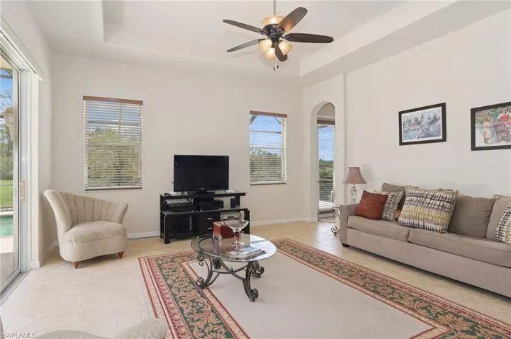 Living area featuring light tile patterned floors, a tray ceiling, arched walkways, and ceiling fan