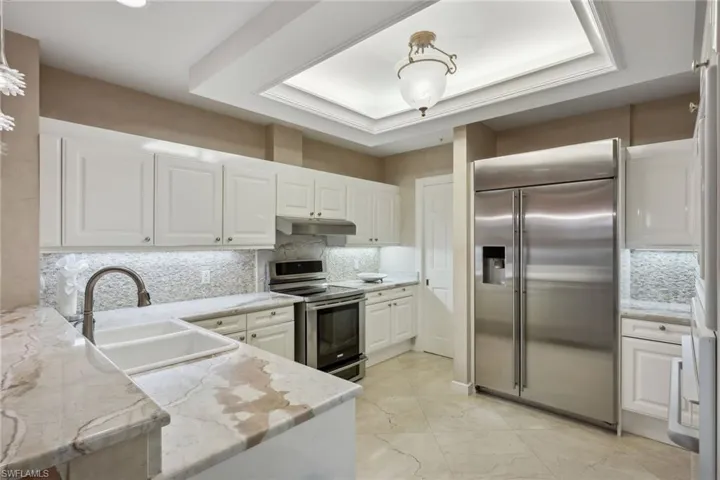 Kitchen with a raised ceiling, white cabinetry, sink, light stone counters, and stainless steel appliances