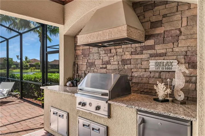 Summer kitchen with granite, stacked stone, fridge, and storage.