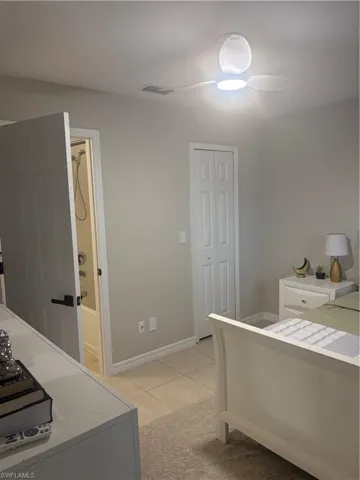 Bedroom with light tile patterned floors, a closet, ensuite bath, and ceiling fan