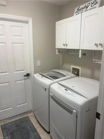 Washroom featuring cabinet space, washing machine and dryer, and light tile patterned flooring