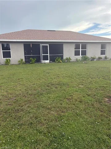 Rear view of property with stucco siding, a lawn, and a shingled roof