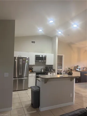 Kitchen featuring fridge, white cabinets, decorative backsplash, light tile patterned flooring, and high vaulted ceiling