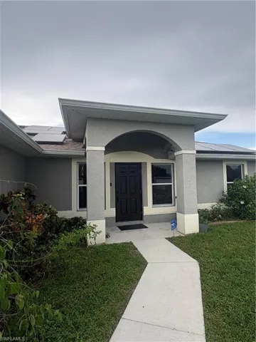 View of exterior entry featuring stucco siding, roof mounted solar panels, and a lawn