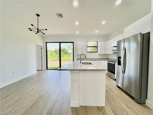 Kitchen featuring light hardwood / wood-style floors, a kitchen island with sink, sink, stainless steel appliances, and white cabinetry