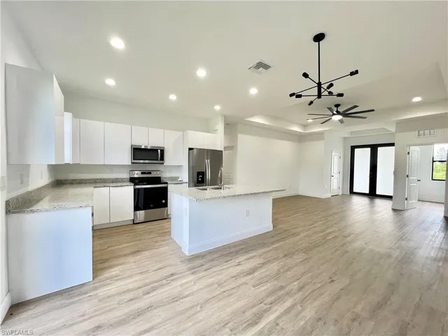 Kitchen with white cabinets, a kitchen island, light hardwood / wood-style flooring, decorative light fixtures, and appliances with stainless steel finishes