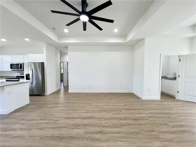 Unfurnished living room with ceiling fan, sink, light wood-type flooring, and a raised ceiling