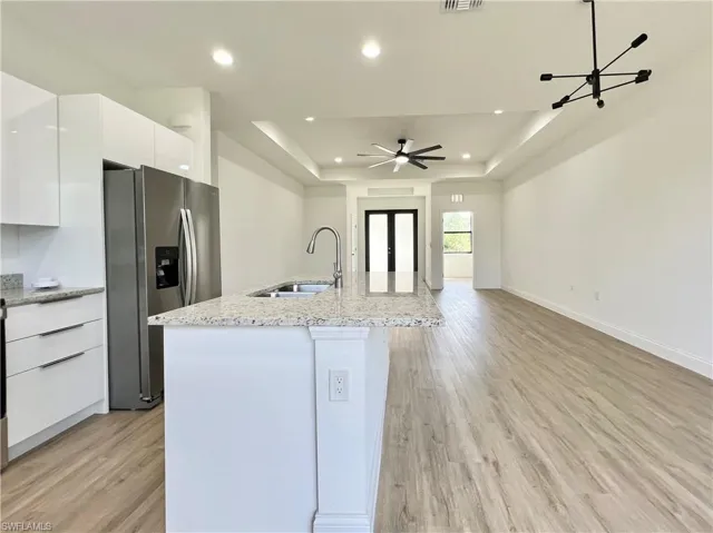 Kitchen featuring a center island with sink, light wood-type flooring, stainless steel fridge with ice dispenser, and white cabinetry