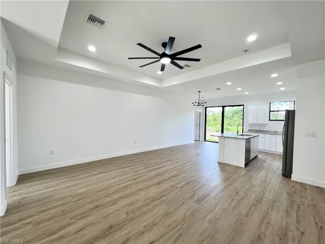Unfurnished living room with light hardwood / wood-style floors, a tray ceiling, and sink