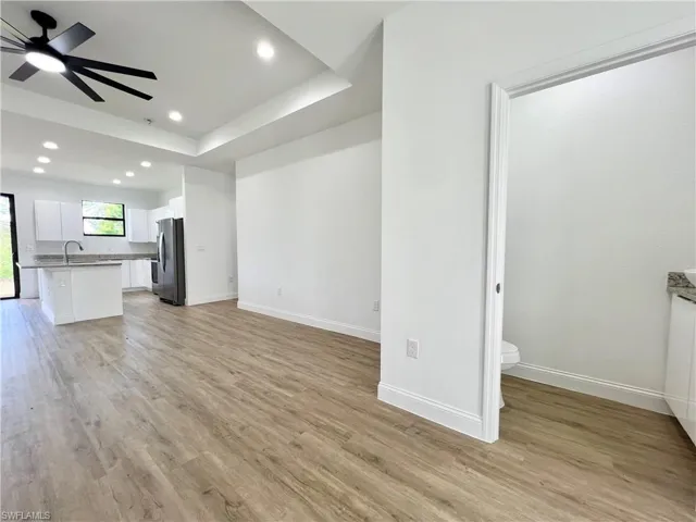 Unfurnished living room with a raised ceiling, light hardwood / wood-style floors, sink, and ceiling fan