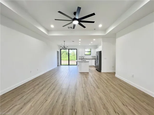 Unfurnished living room with ceiling fan with notable chandelier, light wood-type flooring, sink, and a raised ceiling