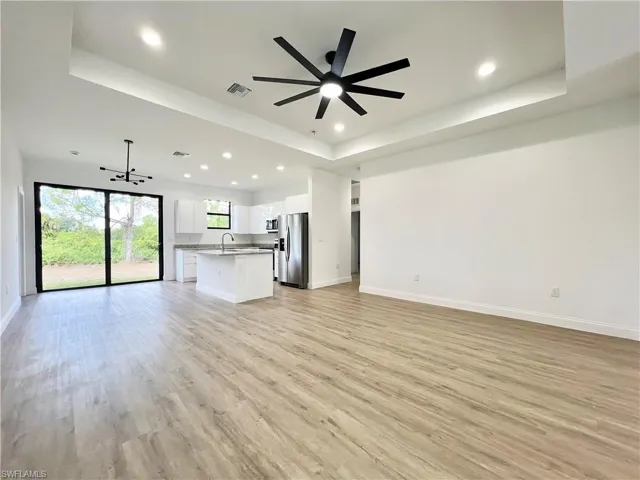 Unfurnished living room with sink, light wood-type flooring, and a tray ceiling