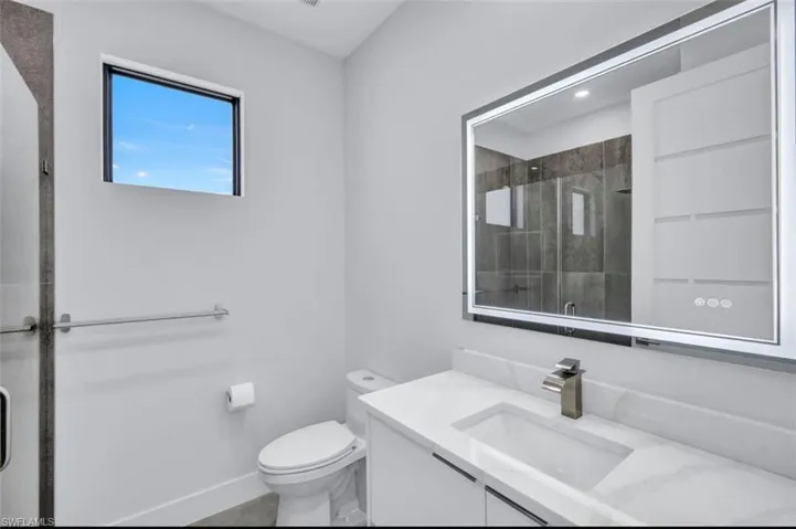 Bathroom featuring toilet, vanity, and a shower with shower door