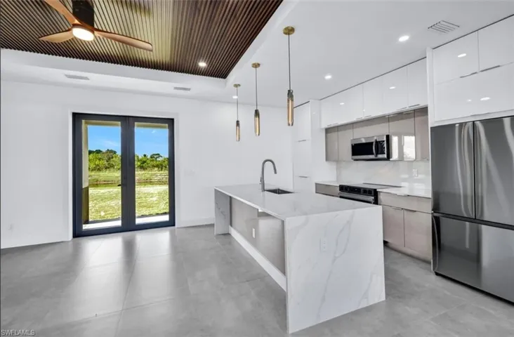 Kitchen featuring stainless steel appliances, white cabinets, a kitchen island with sink, backsplash, and decorative light fixtures