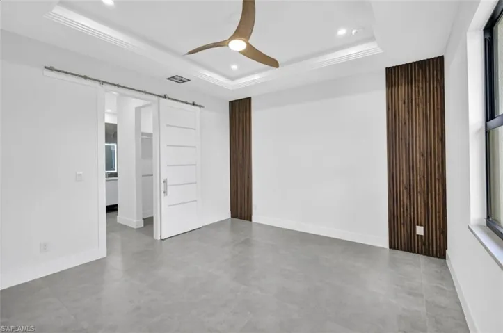 Spare room with a barn door, ceiling fan, and a tray ceiling