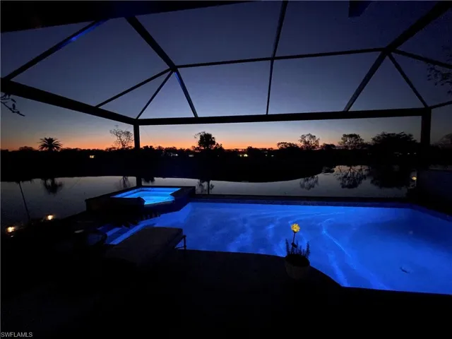 Pool at dusk featuring a pool with connected hot tub, a patio area, and a lanai