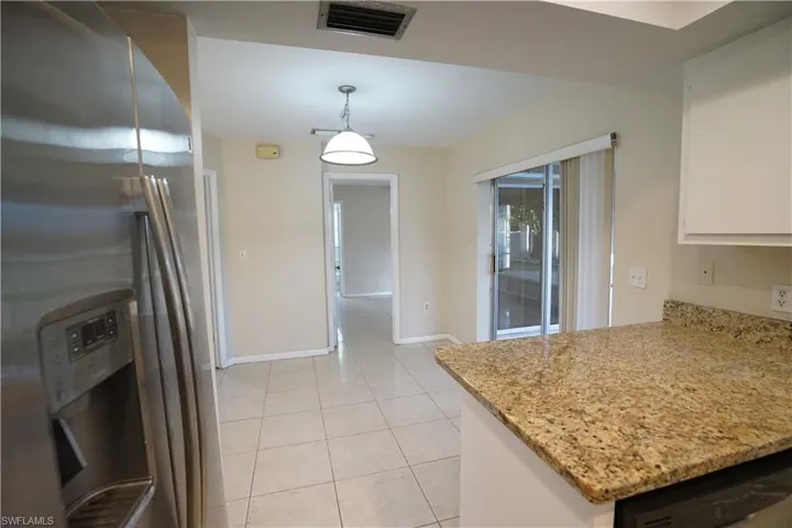 Kitchen with stainless steel refrigerator with ice dispenser, light tile patterned floors, light stone countertops, and white cabinets