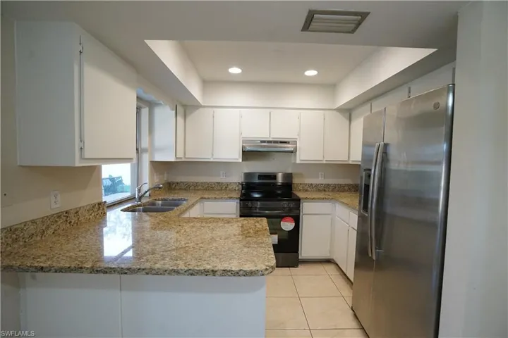 Kitchen with stainless steel fridge with ice dispenser, electric range, white cabinetry, a peninsula, and light stone counters