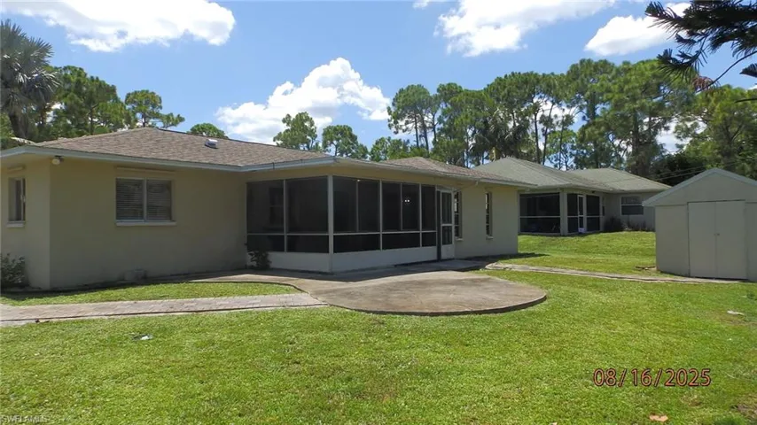 Back of house with stucco siding, roof with shingles, a sunroom, and a lawn