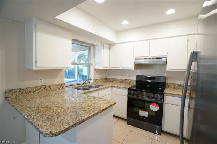 Kitchen featuring black electric range oven, freestanding refrigerator, light stone countertops, a peninsula, and white cabinetry