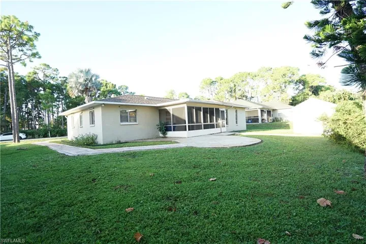 Rear view of house featuring a sunroom, a yard, and stucco siding