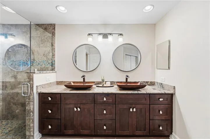 The primary bath, freshly painted in soft neutral tones, showcases dual vessel sinks set atop a comfort-height granite vanity, along with a spacious walk-in shower featuring a sleek, seamless glass enclosure.