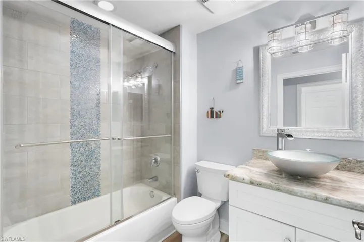 The remodeled second bath showcases a shower–tub combination with a sleek glass enclosure, complemented by a striking listello accent, granite countertop, and an elegant vessel sink.