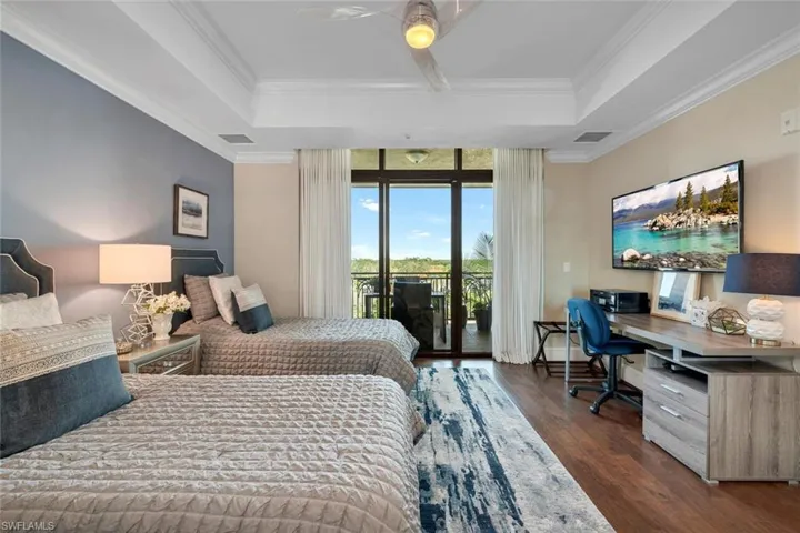 Bedroom with a tray ceiling, ceiling fan, dark wood-type flooring, and access to outside