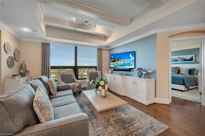 Living room with a tray ceiling, crown molding, dark hardwood / wood-style flooring, and rail lighting
