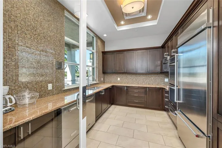 Kitchen with backsplash, sink, light stone countertops, a tray ceiling, and stainless steel appliances