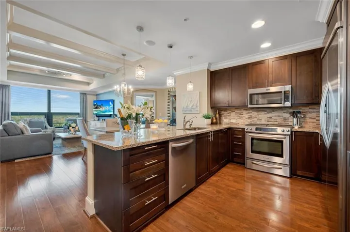 Kitchen featuring kitchen peninsula, appliances with stainless steel finishes, backsplash, light stone countertops, and decorative light fixtures