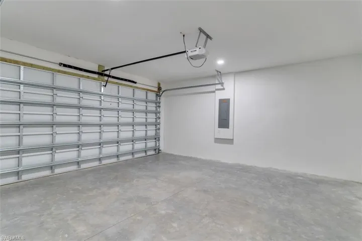Garage featuring electric panel, a garage door opener, and recessed lighting
