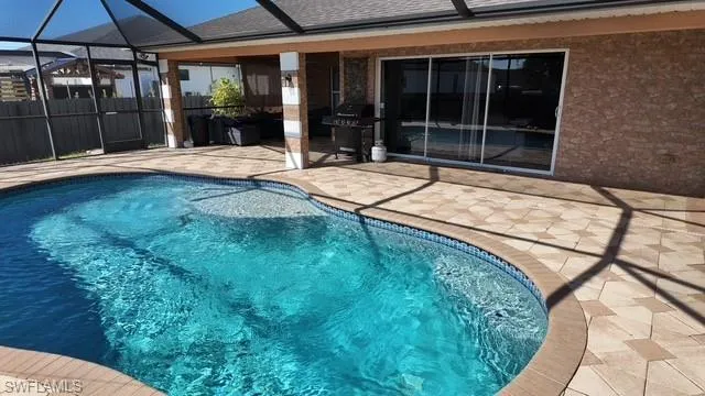 Outdoor pool with a patio area, glass enclosure, a sunroom, and a grill