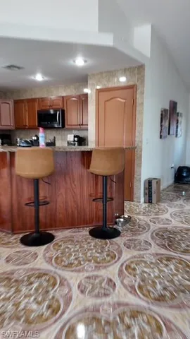 Kitchen featuring a breakfast bar area, wood finish cabinets, stainless steel microwave, and light stone counters