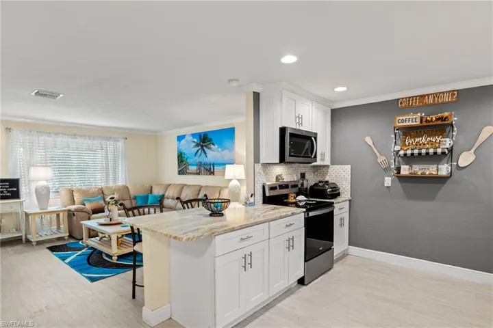 Kitchen with stainless steel appliances, a breakfast bar, white cabinetry, light stone counters, and tasteful backsplash