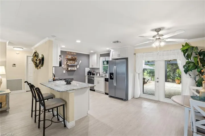 Kitchen with kitchen peninsula, stainless steel appliances, backsplash, light stone countertops, and white cabinetry