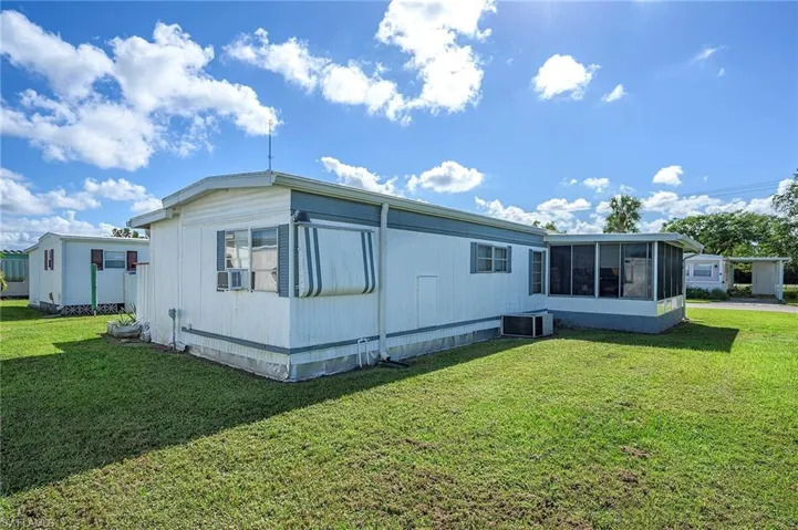 Back of property with central AC unit, cooling unit, a sunroom, and a yard