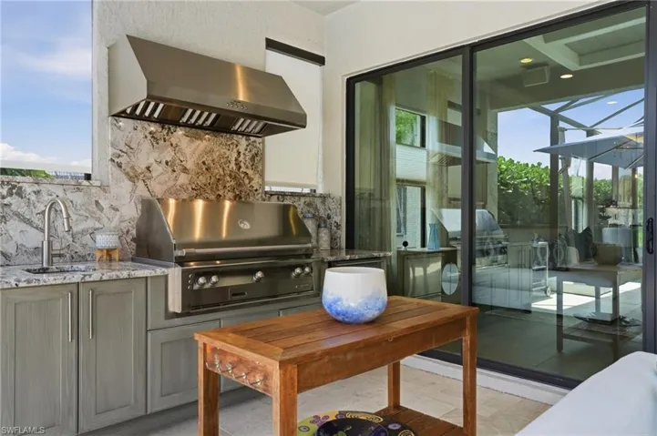 Outdoor kitchen featuring stainless steel grill, coordinating ventilation hood, and a sink with a gooseneck faucet