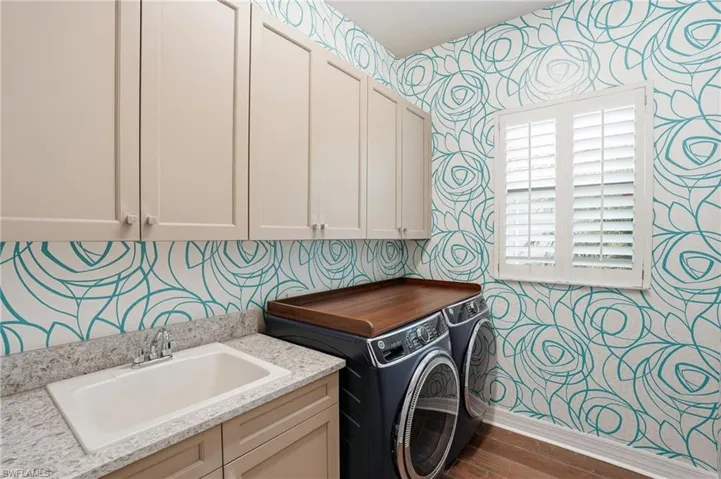 Laundry space featuring a utility sink with a chrome faucet, granite-finish countertop, and neutral cabinetry