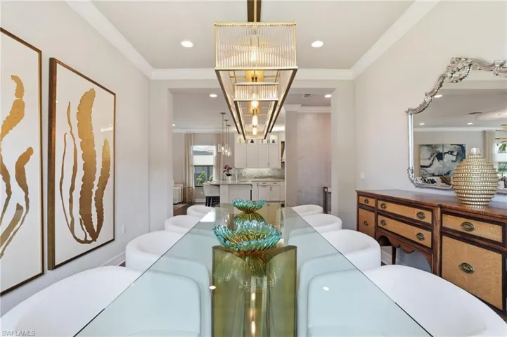 Elongated linear chandelier illuminating a dining area featuring crown molding, recessed lighting, and light-toned wall finishes