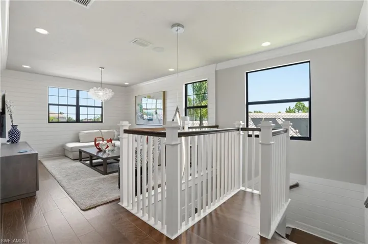 Upper-level landing featuring wood-finish flooring, white spindle railing with a dark wood-finish handrail, and recessed lighting