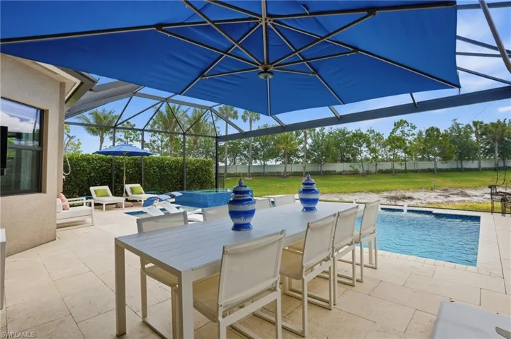 Screened outdoor living area featuring a blue patio umbrella, a rectangular swimming pool, and an integrated spa