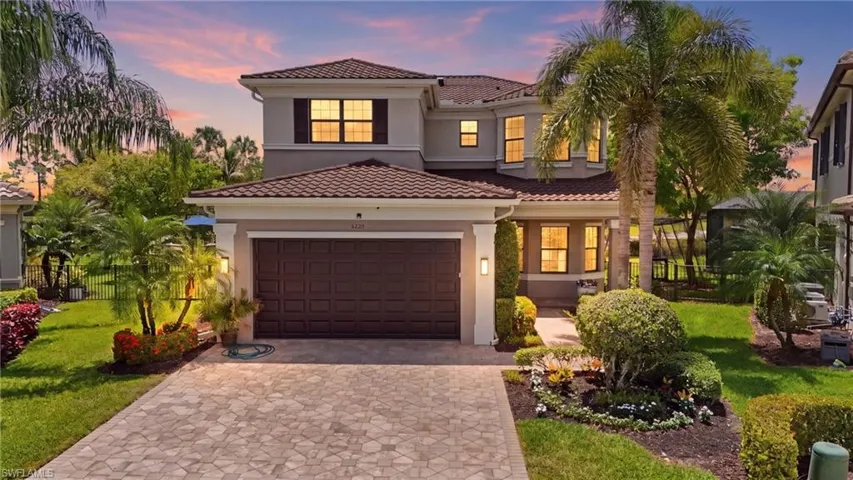 Two-story residence featuring a tile roof, an integrated garage with a decorative door, and a paver driveway