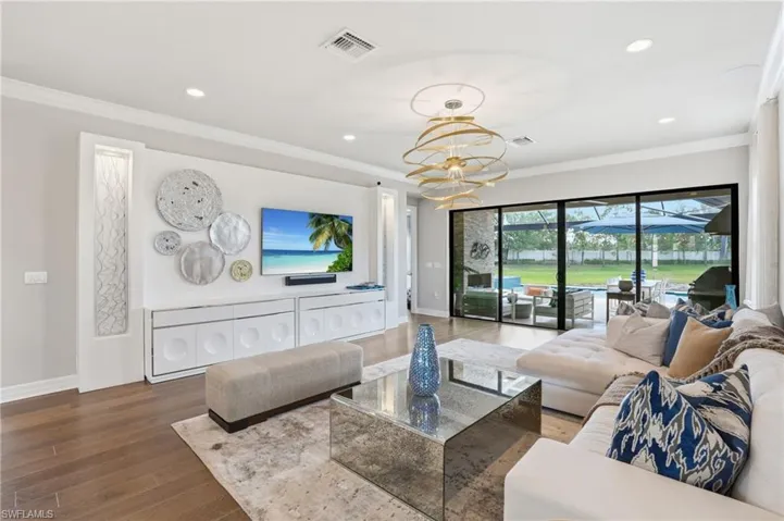 Spacious living area featuring wood-finish flooring, a contemporary ceiling fixture, recessed lighting, and a built-in media console with storage