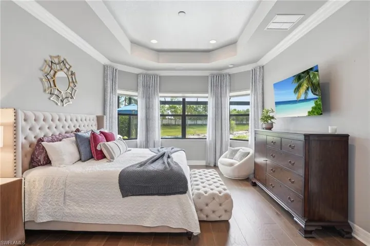 Bedroom featuring a tray ceiling with recessed lighting, wood-finish flooring, and a bay window configuration
