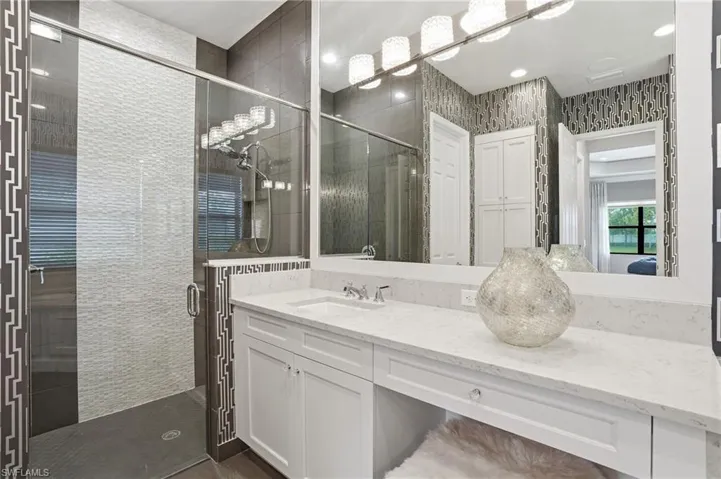 Contemporary bathroom featuring a spacious glass-enclosed shower with textured tile, a white vanity with integrated sink, a large vanity mirror, and modern lighting fixtures