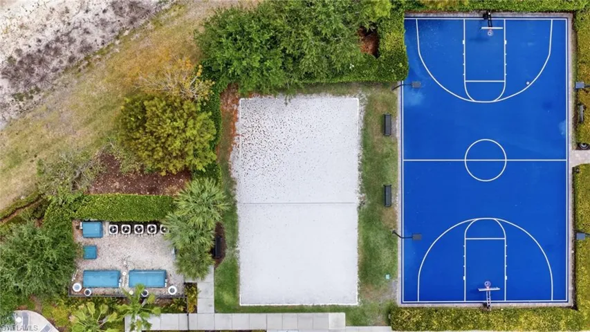 Recreational area featuring a full-size basketball court with a vibrant blue surface, a sand volleyball court, and an outdoor seating area with lounge chairs and sofas