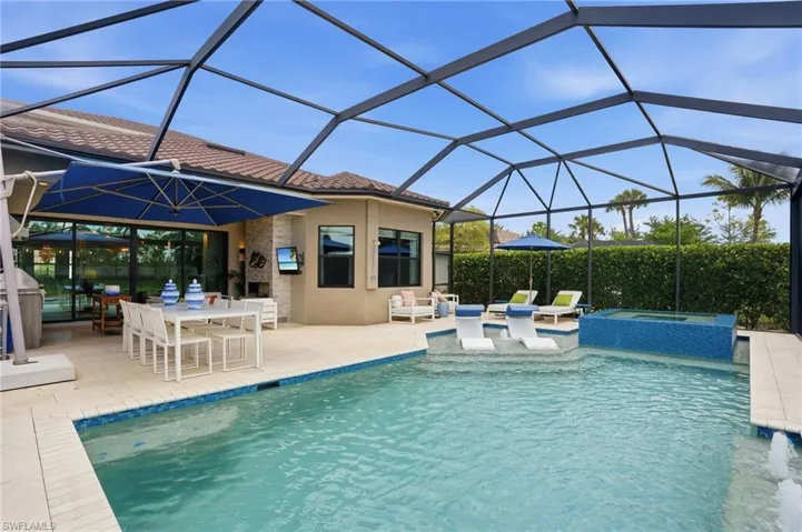 Screened outdoor oasis featuring a private swimming pool, integrated spa with blue tile surround, and an expansive paved patio